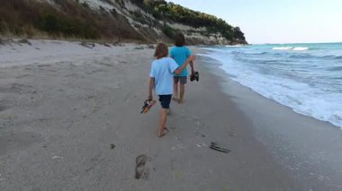 Deniz dalgaları yakınlarındaki kumsalda çıplak ayakla yürüyen iki kardeş, deniz kenarında yaz tatilinin tadını çıkaran kardeşler, aile bağları ve deniz kenarında çocukluk maceraları..
