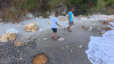Deniz dalgaları yakınlarındaki kumsalda çıplak ayakla yürüyen iki kardeş, deniz kenarında yaz tatilinin tadını çıkaran kardeşler, aile bağları ve deniz kenarında çocukluk maceraları..