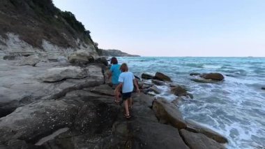 Okyanus dalgaları yakınında deniz kıyısında yürüyen iki kardeş, kıyıları keşfeden kardeşler, deniz kenarında aile tatili, çocukluk bağı ve doğada özgürlük..