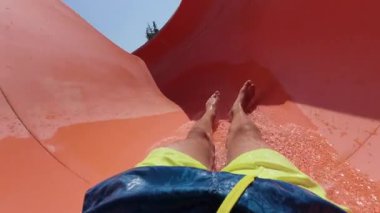 Güneşli bir yaz gününde turuncu su kaydırağından kayarak kayan ve Aquapark 'taki kıvrımlardan geçen kişinin POV videosu..