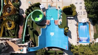Aerial view of a colorful water park with multiple slides, pools, and people enjoying summer activities on a sunny day.