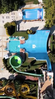Aerial view of a colorful water park with multiple slides, pools, and people enjoying summer activities on a sunny day.