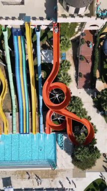 Aerial view of a colorful water park with multiple slides, pools, and people enjoying summer activities on a sunny day.