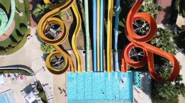 Aerial view of a colorful water park with multiple slides, pools, and people enjoying summer activities on a sunny day.