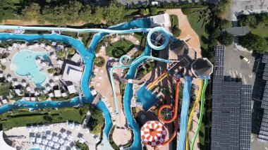 Renkli slaytlarla, tembel nehirlerle, havuzlarla ve dinlenme yerleriyle dolu canlı bir su parkının hava görüntüleri. Aileler ve turistler, modern bir tatil köyünde yaz eğlencesinin tadını çıkarıyorlar..