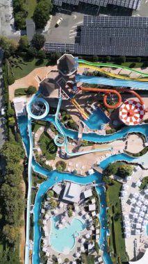 Renkli slaytlarla, tembel nehirlerle, havuzlarla ve dinlenme yerleriyle dolu canlı bir su parkının hava görüntüleri. Aileler ve turistler, modern bir tatil köyünde yaz eğlencesinin tadını çıkarıyorlar..