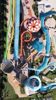 Renkli slaytlarla, tembel nehirlerle, havuzlarla ve dinlenme yerleriyle dolu canlı bir su parkının hava görüntüleri. Aileler ve turistler, modern bir tatil köyünde yaz eğlencesinin tadını çıkarıyorlar..