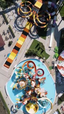 Renkli slaytlarla, tembel nehirlerle, havuzlarla ve dinlenme yerleriyle dolu canlı bir su parkının hava görüntüleri. Aileler ve turistler, modern bir tatil köyünde yaz eğlencesinin tadını çıkarıyorlar..