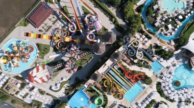 Renkli slaytlarla, tembel nehirlerle, havuzlarla ve dinlenme yerleriyle dolu canlı bir su parkının hava görüntüleri. Aileler ve turistler, modern bir tatil köyünde yaz eğlencesinin tadını çıkarıyorlar..