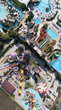 Renkli slaytlar, havuzlar, sıçrama bölgeleri ve rahatlama alanlarıyla dolu devasa bir su parkının çarpıcı görüntüsü. İnsanlar heyecan ve eğlence dolu güneşli bir günün tadını çıkarırlar..