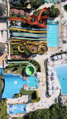 Renkli slaytlar, havuzlar, sıçrama bölgeleri ve rahatlama alanlarıyla dolu devasa bir su parkının çarpıcı görüntüsü. İnsanlar heyecan ve eğlence dolu güneşli bir günün tadını çıkarırlar..