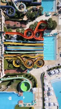 Renkli slaytlar, havuzlar, sıçrama bölgeleri ve rahatlama alanlarıyla dolu devasa bir su parkının çarpıcı görüntüsü. İnsanlar heyecan ve eğlence dolu güneşli bir günün tadını çıkarırlar..