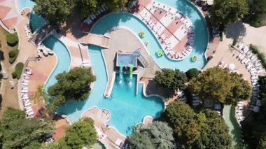 Güneşli bir yaz günü güneşli bir günde güneşli yataklar ve ağaçlarla çevrili havuz, tembel nehirler ve küçük slaytlarla dolu rahatlatıcı bir su parkı manzarası..