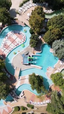 Güneşli bir yaz günü güneşli bir günde güneşli yataklar ve ağaçlarla çevrili havuz, tembel nehirler ve küçük slaytlarla dolu rahatlatıcı bir su parkı manzarası..