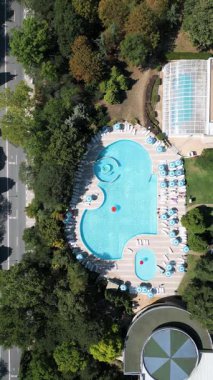 Güneşli bir yaz günü güneşli bir tatil köyünde yeşillik içinde güneşlenen güneşli şezlonglar ve şemsiyelerle çevrili sessiz bir açık yüzme havuzu manzarası..