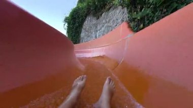 Güneşli bir yaz gününde turuncu su kaydırağından kayarak kayan ve Aquapark 'taki kıvrımlardan geçen kişinin POV videosu..