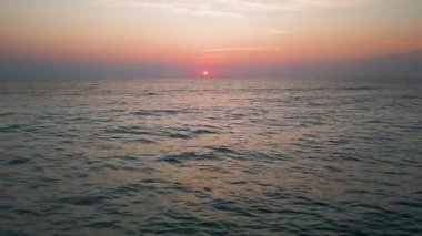 Peaceful aerial view of a calm sea at sunrise with soft pastel colors reflecting on the water. Tranquil morning seascape captured from a drone.