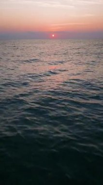 Peaceful aerial view of a calm sea at sunrise with soft pastel colors reflecting on the water. Tranquil morning seascape captured from a drone.