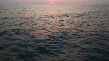 Peaceful aerial view of a calm sea at sunrise with soft pastel colors reflecting on the water. Tranquil morning seascape captured from a drone.