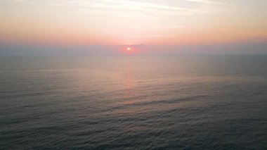 Peaceful aerial view of a calm sea at sunrise with soft pastel colors reflecting on the water. Tranquil morning seascape captured from a drone.
