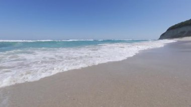 Slow motion footage of a powerful sea wave breaking near the camera under a clear blue sky. Crystal clear turquoise water and foamy splash in bright daylight.