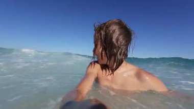 Slow motion video of a happy boy splashing water in the sea, smiling at the camera on a bright sunny day. Pure joy and summer fun at the beach, captured in vivid detail.