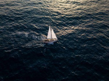 Aerial video of a white sailboat sailing alone on deep blue sea. Calm waves shimmer under sunlight. Peaceful and adventurous maritime scene perfect for travel and freedom themes.