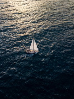 Aerial video of a white sailboat sailing alone on deep blue sea. Calm waves shimmer under sunlight. Peaceful and adventurous maritime scene perfect for travel and freedom themes.