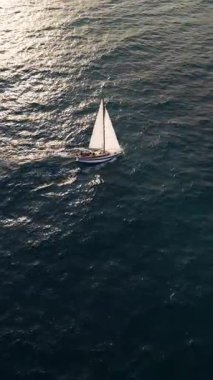 Aerial video of a white sailboat sailing alone on deep blue sea. Calm waves shimmer under sunlight. Peaceful and adventurous maritime scene perfect for travel and freedom themes.