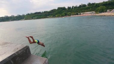 Slow motion video of an 11-year-old boy diving into the sea from a pier on a summer day, enjoying freedom, vacation and adventure outdoors.