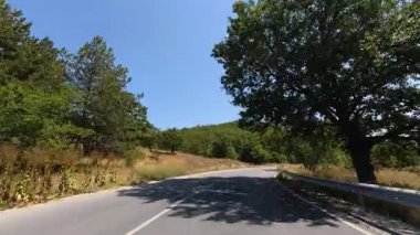 Driving along empty country road towards a green hill, surrounded by golden hay fields under clear blue sky. Scenic rural travel video.