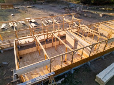 Aerial view of wooden house construction in progress. Framework and walls being built with timber, showing structure and building process.