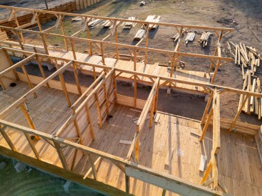 Aerial view of wooden house construction in progress. Framework and walls being built with timber, showing structure and building process.