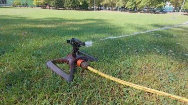 Slow motion of garden sprinkler spraying water on green lawn, irrigation system watering grass in summer backyard.