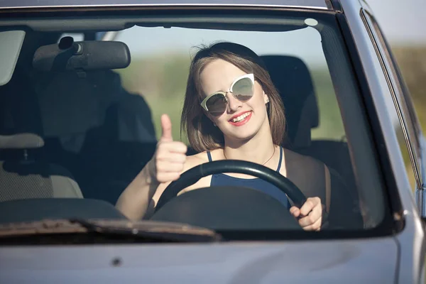 彼女の手を上げられた指で車のホイールの後ろに笑顔で美しい少女 — ストック写真