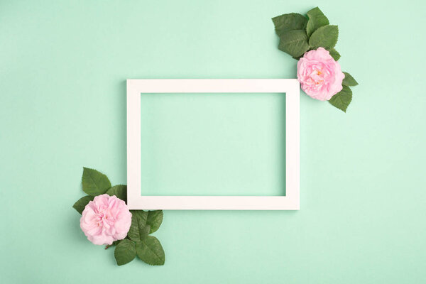 Beautiful rose flowers and blank frame on pastel mint background. Soft light color. Top view, copy space.