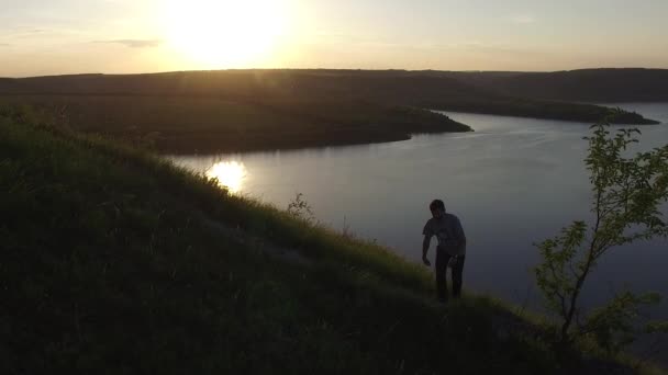 Tiro épico aéreo de um homem caminhando na borda da margem do rio como uma silhueta em belo pôr do sol . — Vídeo de Stock