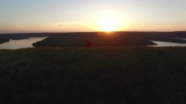 Hava uçuş nehir banka kenarında ellerinde aşık onun mutlu kadın büküm adam yukarıda. Şaşırtıcı kırmızı elbiseli kadın. Siyah adam. Günbatımı.