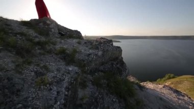 Güzel Avrupa kadın büyük nehir banka kenarında kırmızı elbise ile oynarken. Etkileyici bir geçmiş. Büyük nehir. Günbatımı.