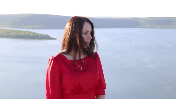Schöne Europäerin in rotem Kleid blickt zur Seite am Ufer des Flusses. Erstaunlicher Hintergrund. Riesenfluss. Sonnenuntergang. — Stockvideo