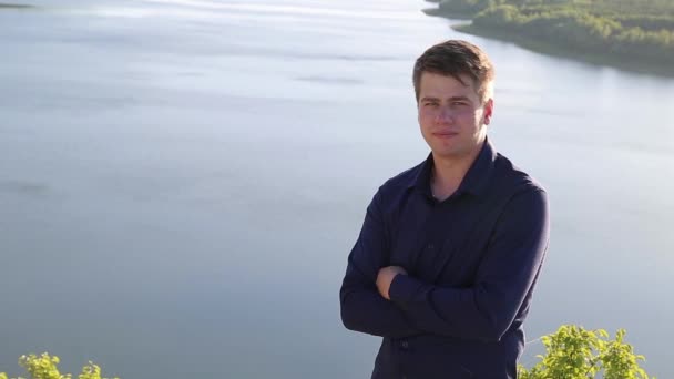 Portret van aantrekkelijke jongeman fixing zijn haar voor de camera op de enorme rivier hight banken rand. — Stockvideo