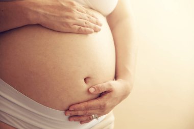 Genç hamile kadın elleri şişmiş karnı üzerinde tutar. Hazırlık ve beklenti kavramı. yakın çekim. kopya alanı ile yatay