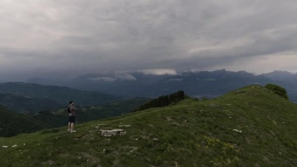Турист, стоящий на скале и смотрящий на панораму гор — стоковое видео