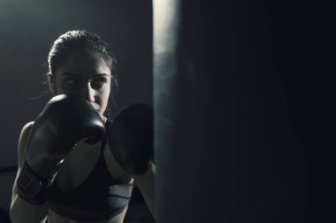 Genç kadının eğitim boks salonunda yapması o giyiyor boks eldivenleri ve kum torbası isabet