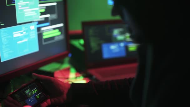 专业黑客使用多个设备 他正在检查计算机屏幕上的数据传输和他的智能手机 — 图库视频影像