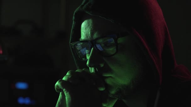 黑客戴着眼镜和帽衫 他正在看着电脑屏幕上运行的代码 对着相机 网络犯罪和黑客的概念大喊大叫 — 图库视频影像