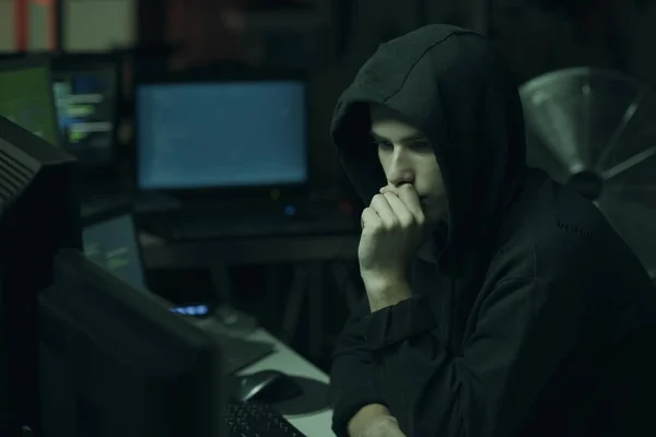 年轻的黑客与帽衫的手在下巴和工作与计算机 技术和网络犯罪的概念 — 图库照片