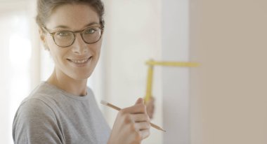 Gülümseyen genç kadın bir ev makyaj yapıyor, o katlanan bir cetvel, DIY ve ev yenileme kavram kullanarak bir duvar ölçmek