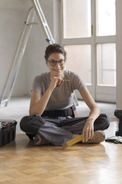 Çekici bir ev yenileme üzerinde çalışan kadın gülümseyerek, araçları ve poz, house tadilat kavramı ile katta oturuyor