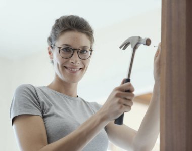 Woman repairing a door at home using a hammer: home renovation and DIY concept clipart